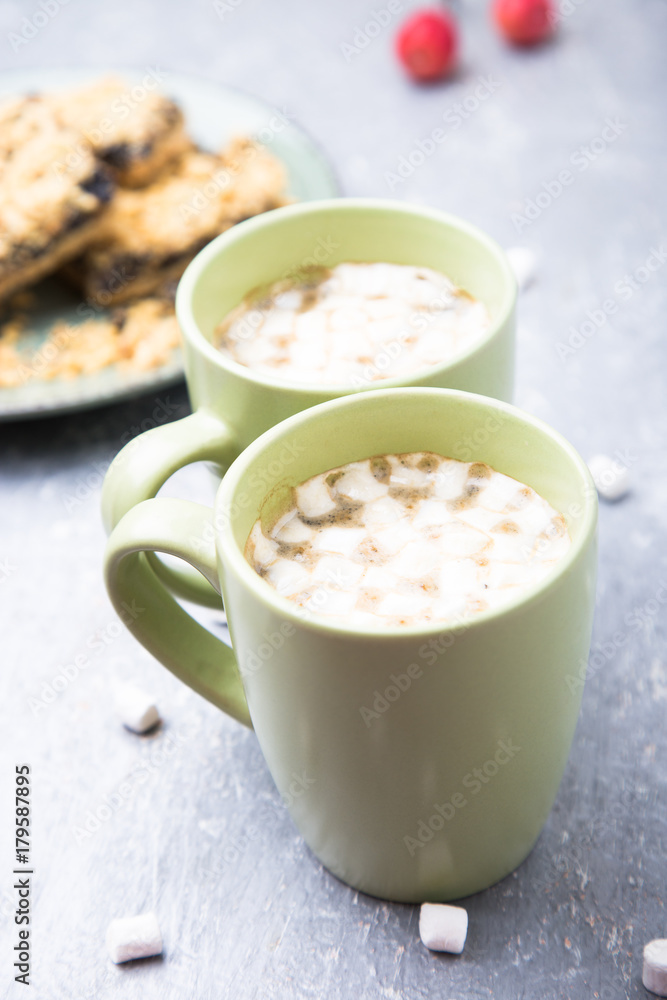 Two cup of hot coffee or chocolate and cake with marshmallow on grey background. Closeup. Two cup of hot coffee or chocolate and cake with marshmallow on grey background. Closeup.