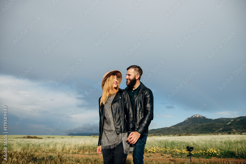 Happy loving couple walking around the field holding hands, mountains on the background