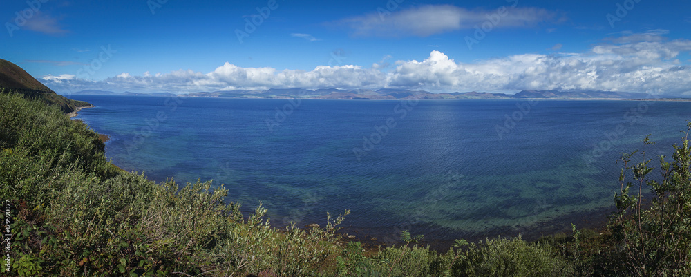 Vue panoramique dans le comté de l'anneau du Kerry. Un bras de mer, avec au fond des collines ensoleillées et ruban de nuages. Au premier plan la plage et de la verdure