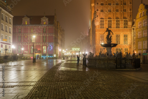Beautifully illuminated Old Town in Gdansk with fountain of the Neptune. Foggy night. Poland.