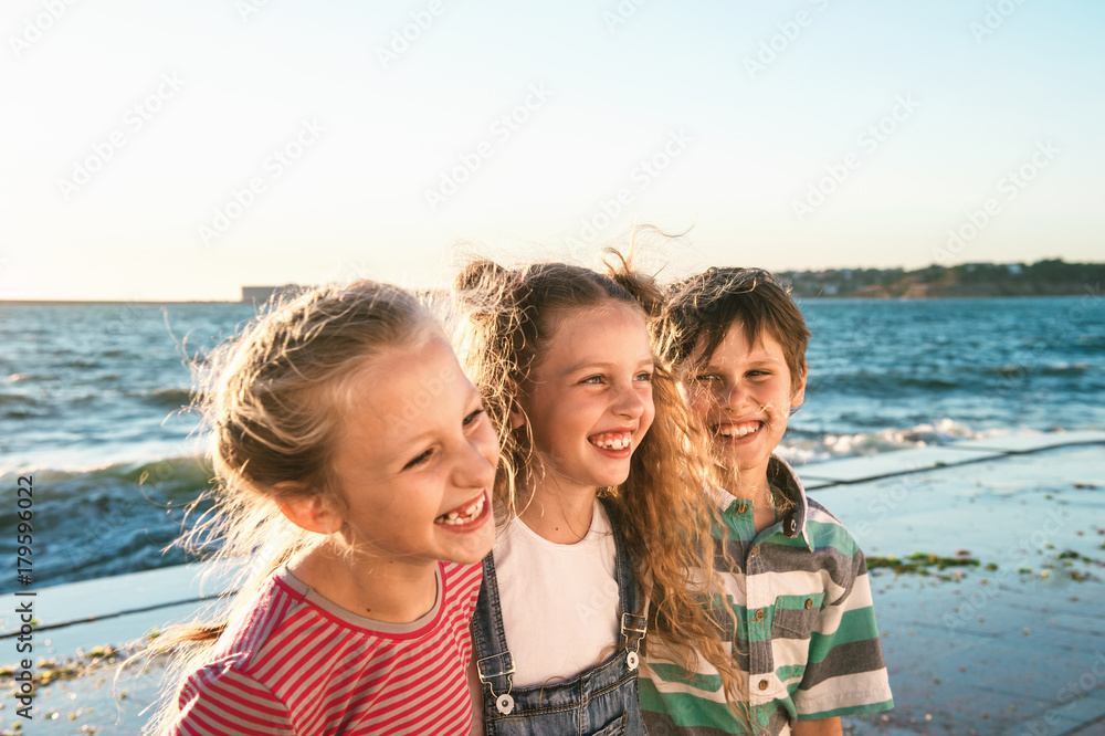 Close up portrait of three happy teenage kids walk along the waterfront and laughing