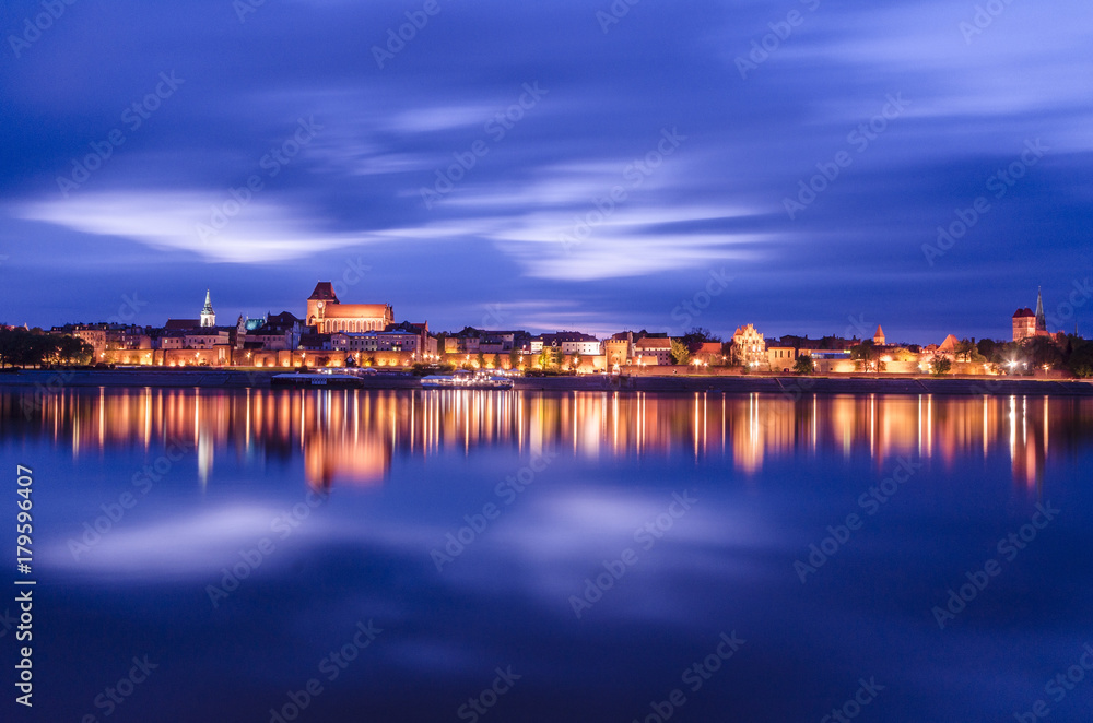 Torun at night. UNESCO-class medieval Old Town reflected in Vistula river, Poland. Europe.