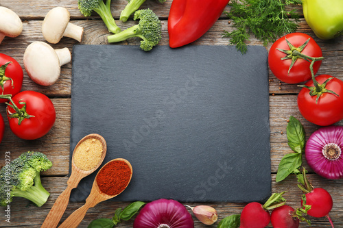 Black cutting board with vegetables and spices on wooden table