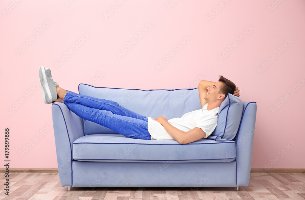 Young man on blue sofa near color wall