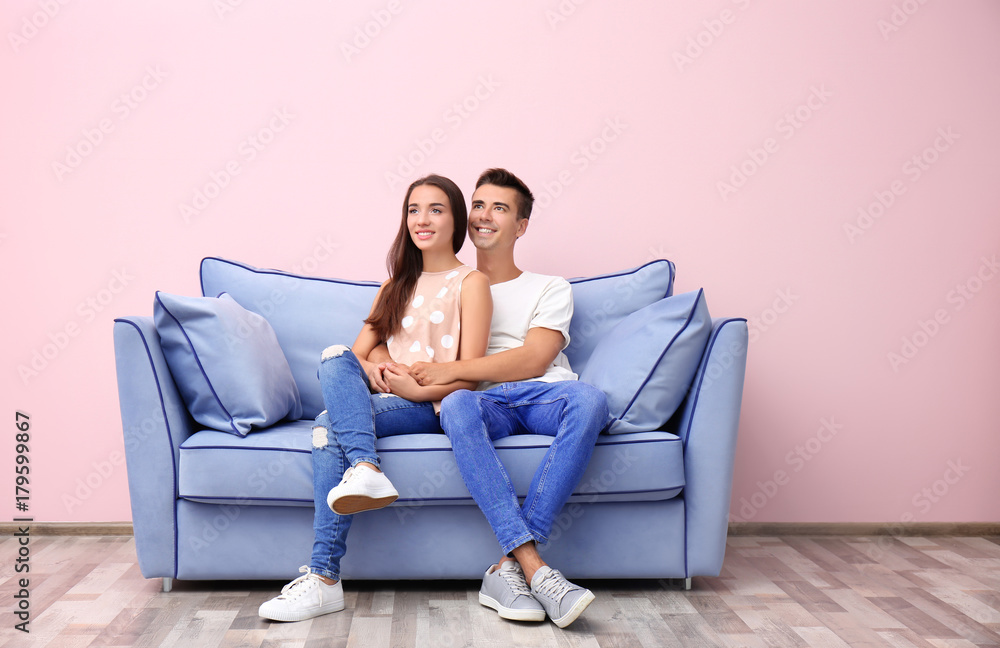 Young couple on blue sofa near color wall Young couple on blue sofa near color wall