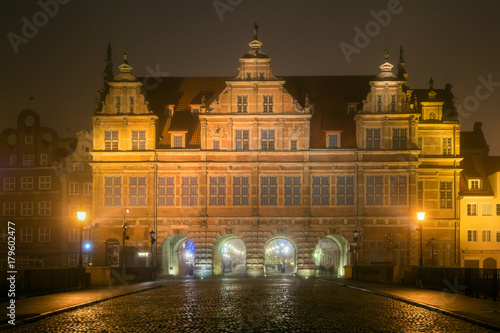 Cobblestone street and historic Green Gate in Old Town of Gdansk in the fog at night. Poland.