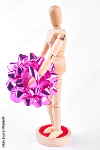 Wooden dummy holding pink bow. Human wooden mannequin with gift bow isolated on white background, side profile. Holidays and celebrations concept. © DenisProduction.com