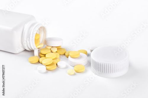 Pills and bottle, white background. Yellow pills and white plastic pills bottle isolated on white background.