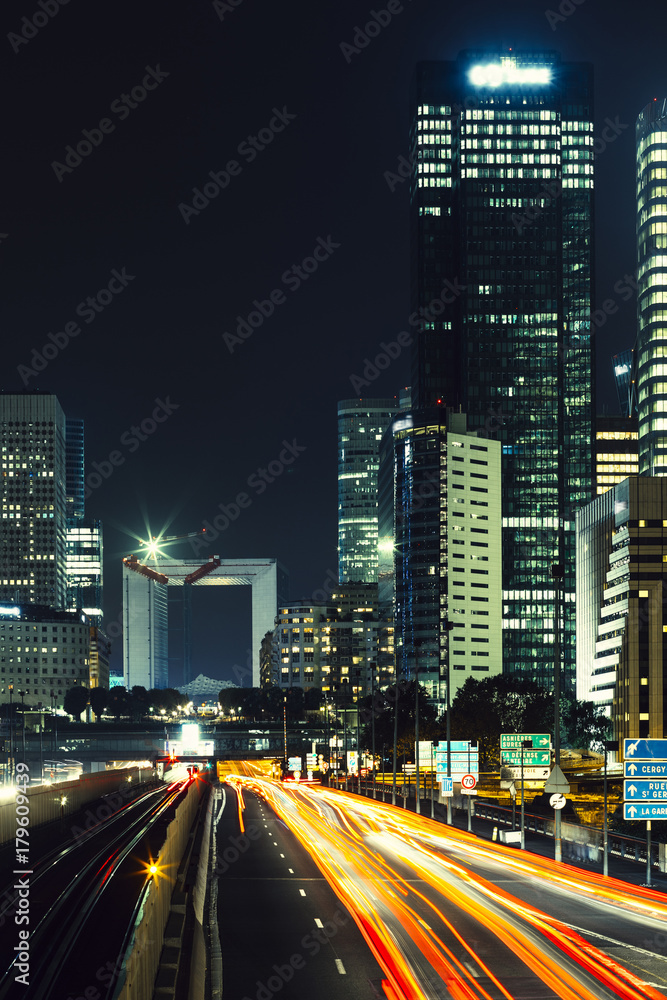 Obraz premium Skyscrapers in Paris business district La Defense. European night cityscape with dynamic street traffic, car lights and glass facades of modern buildings. Economy, finances, transport concept. Toned