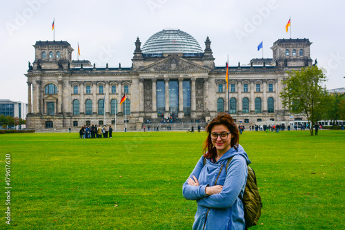Young woman wearing glasses with backpack in front of the Bundestag building in Berlin. Erasmus student, studying abroad and tourist concept.