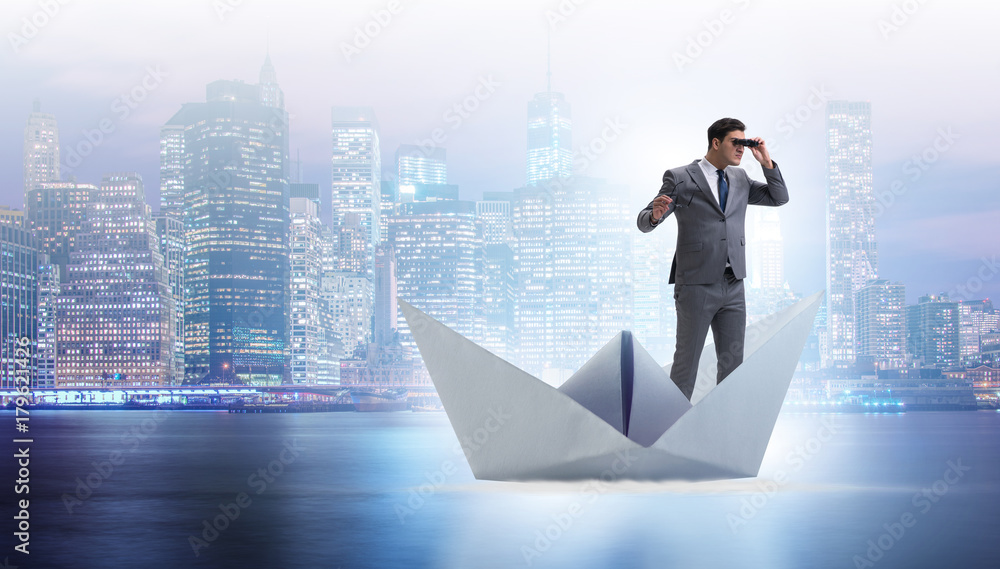 Businessman looking into future with binoculars in paper ship bo Businessman looking into future with binoculars in paper ship bo
