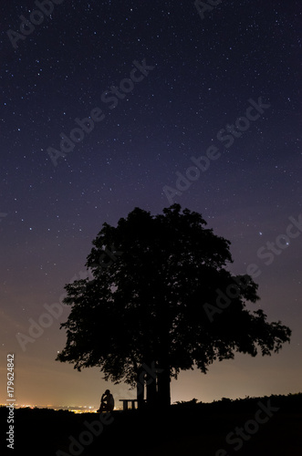 Silhouette of a man sitting and thinking under the tree at starry night