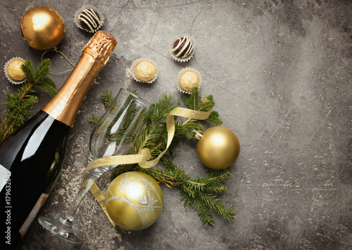 A bottle of champagne with various chocolate candies of a round shape an empty glass and spruce branches lie on a gray background under the concrete. Celebratory concept.