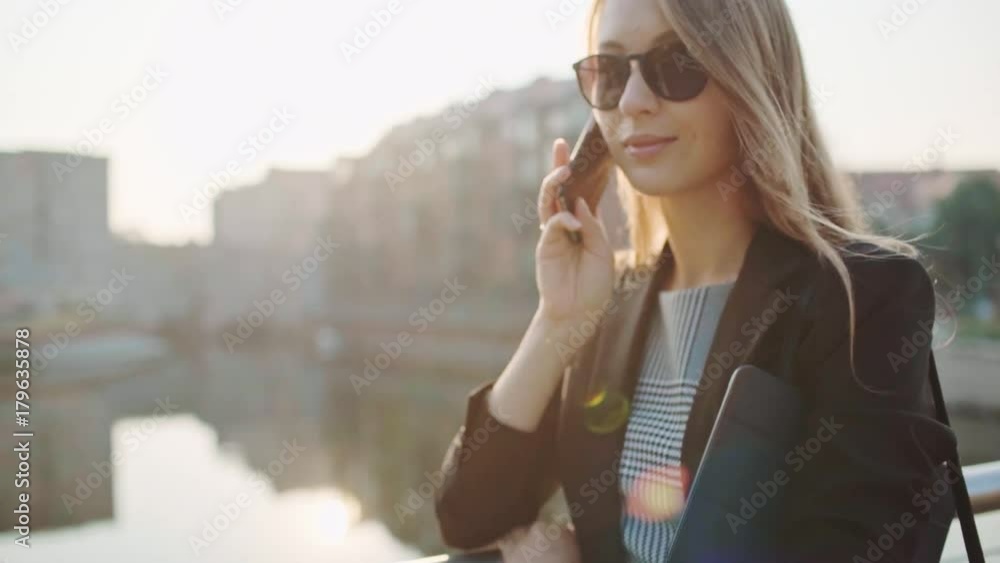 Young Businesswoman Using SmartPhone in the Sunny Morning City. SLOW MOTION. STEADICAM Stabilized Shot. Attractive Professional Business Woman talking on a cell phone in a city. Lens Flare. Young Businesswoman Using SmartPhone in the Sunny Morning City. SLOW MOTION. STEADICAM Stabilized Shot. Attractive Professional Business Woman talking on a cell phone in a city. Lens Flare.