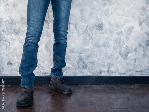 Close up of Man's legs in jeans and boots on wooden floor. Free space for text