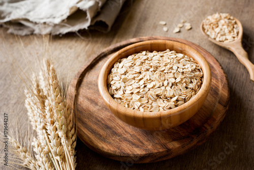 Rolled oats, organic oat flakes in wooden bowl and golden wheat ears on wooden background. Healthy lifestyle, healthy eating, vegan food concept photo