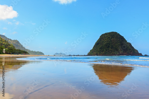 View of Red island beach ( pantai Pulau merah ) in Banyuwangi in Indonesia. Walking along sea surf by empty of people endless sand beach. Java popular travel destination. Summer holiday background.