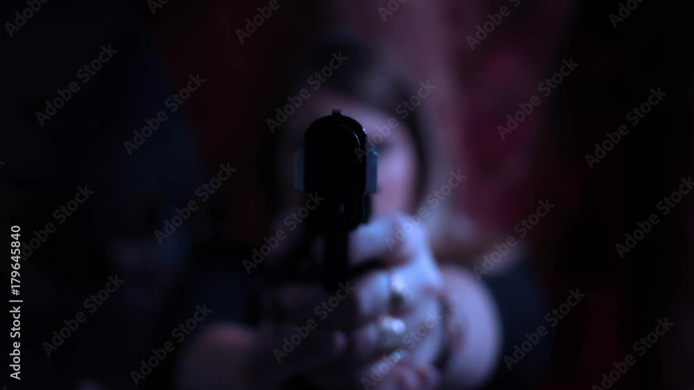 Color graded female assassin aiming pistol at camera in dark cinematic room Color graded female assassin aiming pistol at camera in dark cinematic room