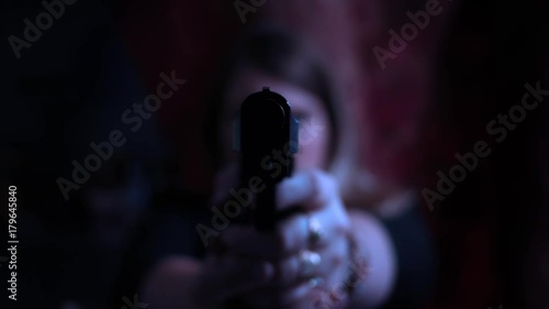 Color graded female assassin aiming pistol at camera in dark cinematic room photo