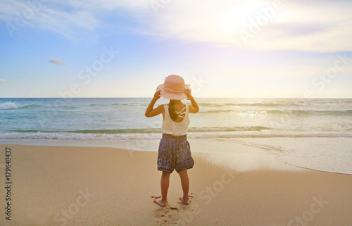 Rear view Adorable little girl wear straw hat relax at the beach at sunset.