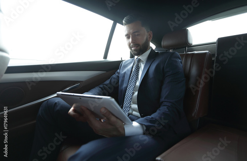 businessman working in the back seat of a car and using a tablet © ASDF