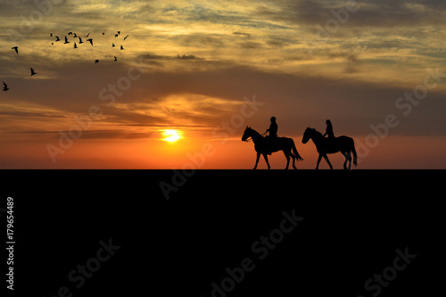 A couple on a horse riders at sunset