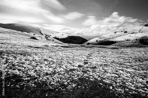 Long exposure photo of a mountain scenery with grass and melting snow, under a deep sky with moving clouds