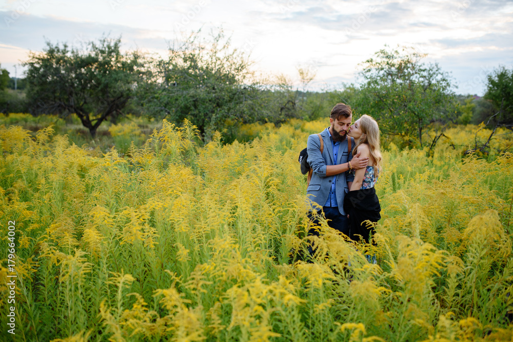 Young couple in love dressed in country style standing on field of flowers Young couple in love dressed in country style standing on field of flowers