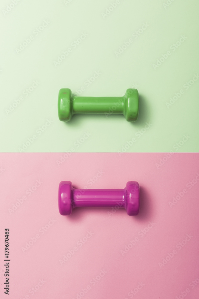 two dumbbell on the color(green, pink) paper background. two dumbbell on the color(green, pink) paper background.