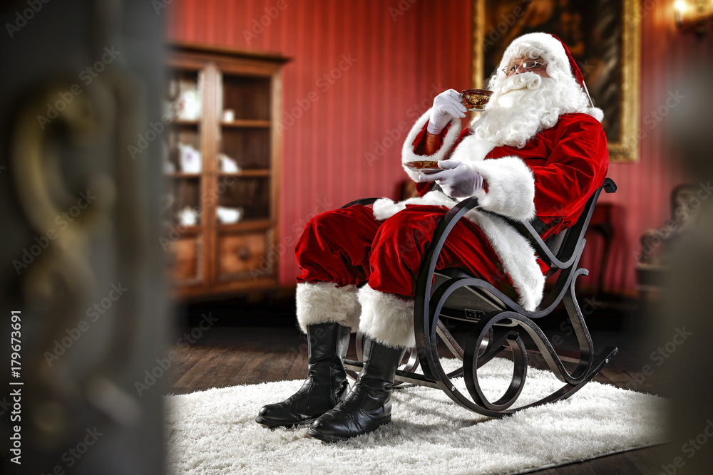 Obraz premium Santa Claus sitting in a wooden chair. Interior of the house with red walls and old furniture. Blurred wall fragments on first background.