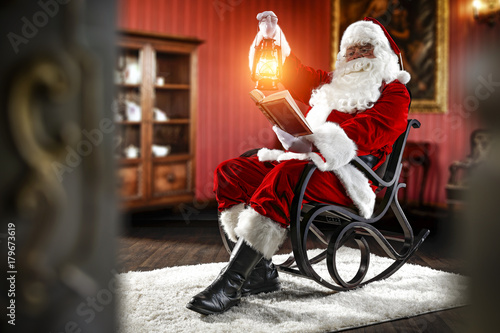 Santa Claus sitting in a wooden chair. Interior of the house with red walls and old furniture. Blurred wall fragments on first background.