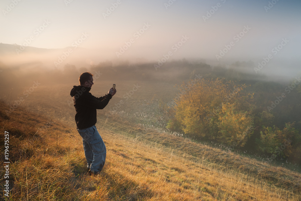 Man is hiking and photographing nature with mobile phone in the morning. 