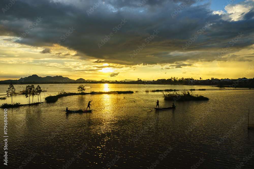 Naklejka premium Sunset on cultivated field with fishermen catching fish by throwing nest in An Giang, south of Vietnam