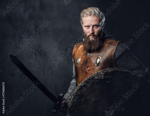 Viking dressed in Nordic armor holds a shield and silver sword.