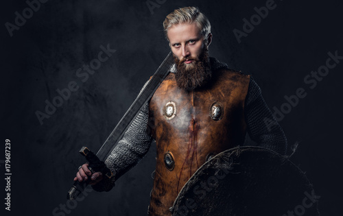 Viking dressed in Nordic armor holds a shield and silver sword.