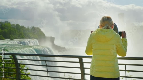 A woman looks at Niagara Falls through a coin operated binoculars. Tourism in the USA concept