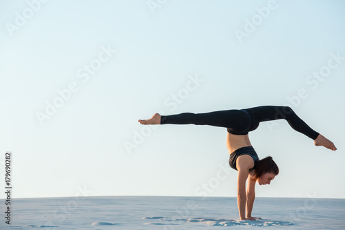 Young woman practicing inversion balancing yoga pose handstand on sand.