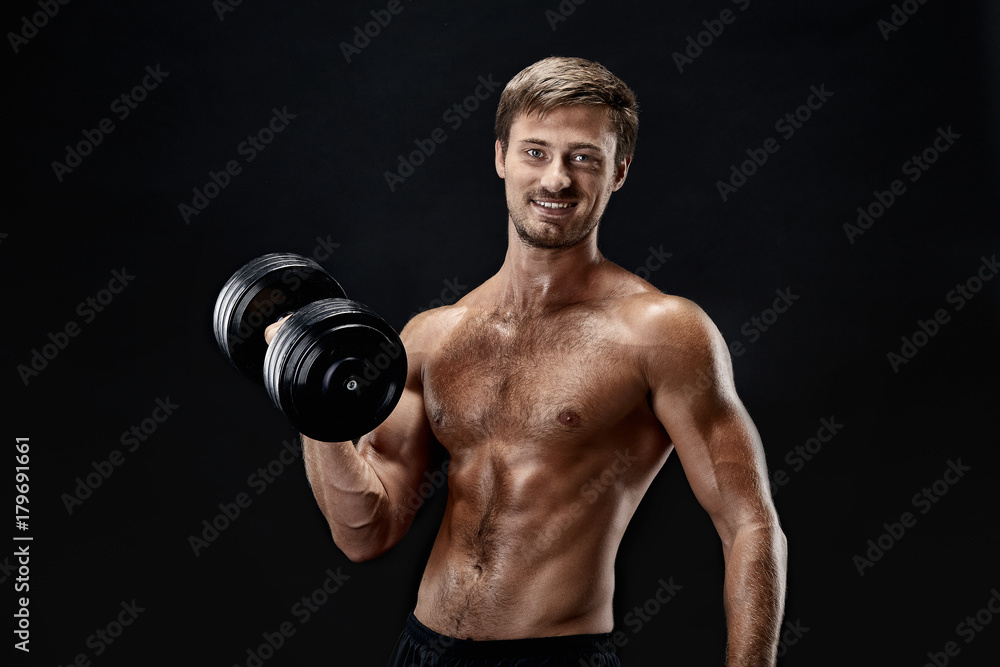 Cropped horizontal shot of a young fit bodybuilder exercising with dumbbells posing on black background