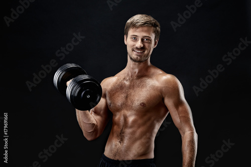 Cropped horizontal shot of a young fit bodybuilder exercising with dumbbells posing on black background © nazarovsergey