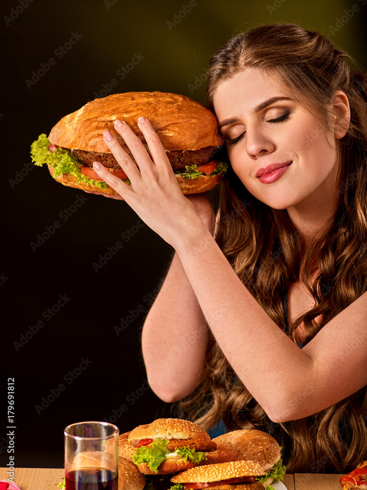 Woman eating french fries and hamburger with pizza. Student consume fast food on table. Girl trying to eat junk on dark background. Cook teaches cook and shares recipes. Dinner for student. Woman eating french fries and hamburger with pizza. Student consume fast food on table. Girl trying to eat junk on dark background. Cook teaches cook and shares recipes. Dinner for student.