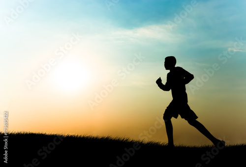 silhouette of a person running towards the setting sun. © Anek