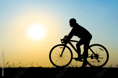 silhouette of young woman cyclist on sunset sky with riding along the prairie at yellow evening horizon sea yellow sunset heaven background Outdoor