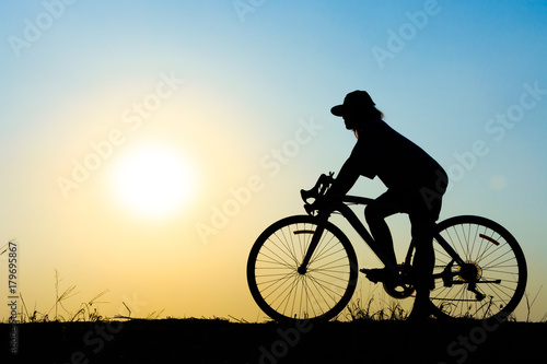 silhouette of young woman cyclist on sunset sky with riding along the prairie at yellow evening horizon sea yellow sunset heaven background Outdoor