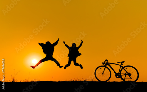 Silhouette of a children jumping on grass with a bicycle.