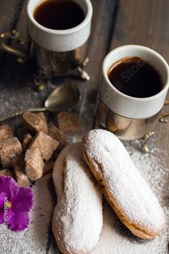 Cake eclair with coffee and cane sugar on a wooden background