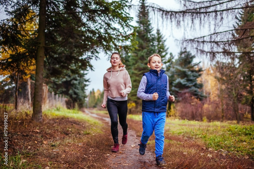Little boy and his sister running in autumn forest