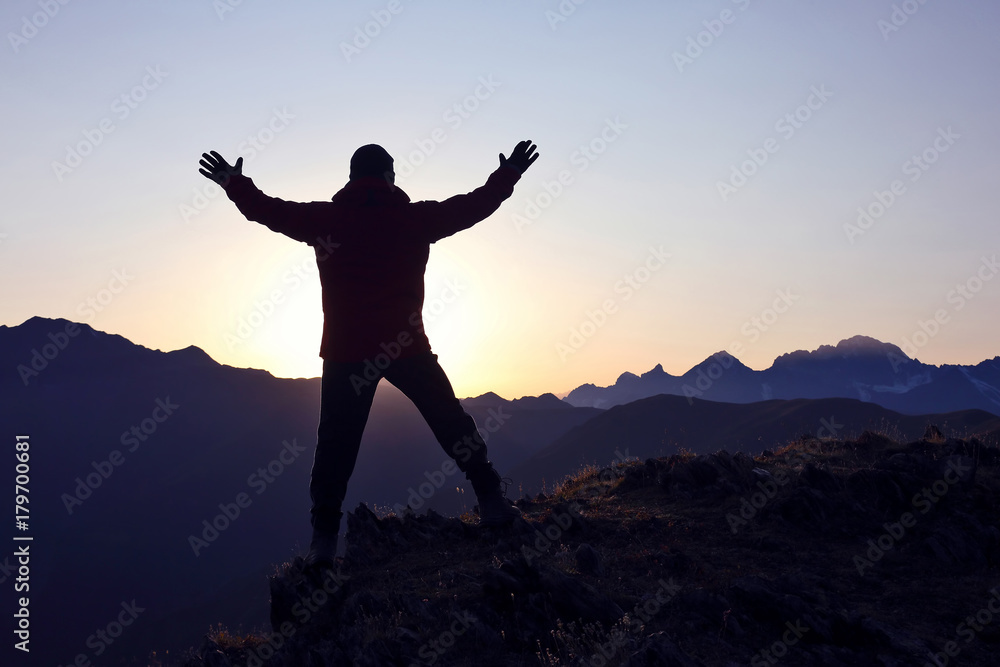 tourist with arms raised standing on the mountain at dawn