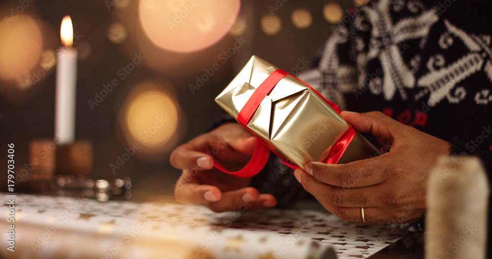 Handsome dark skinned man in black white and red fairisle sweather wrapping Christmas present among decorations and lights Handsome dark skinned man in black white and red fairisle sweather wrapping Christmas present among decorations and lights