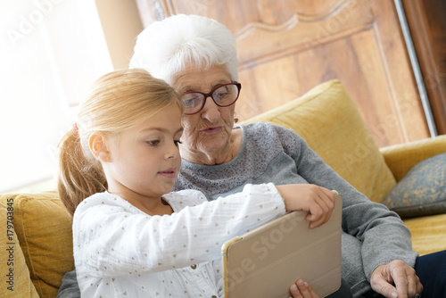 Little girl with grandmother using tablet at home