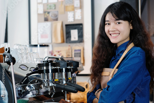 Young asian woman Barista standing with smiling face in font of cafe counter background, small business owner, food and drink industry concept